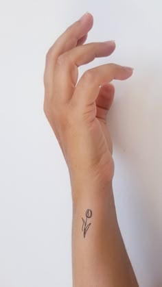 a woman's hand with a small flower tattoo on her left wrist, against a white wall