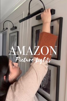 a woman hanging pictures on the wall with an amazon logo above her head and text over it