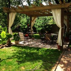 a patio covered in white curtains and furniture next to a table with chairs under it