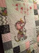 an elephant quilt hanging on the wall next to a bed with pink and green flowers