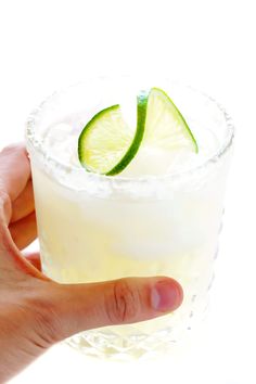 a hand holding a drink with a lime slice on the rim