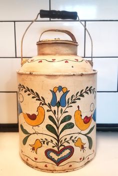 an old white pot with birds painted on it's side and a black handle