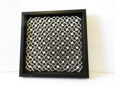 a black and white framed art piece with geometric designs on the front, in a wooden frame