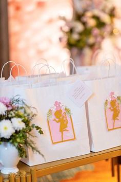 two bags with little tags on them sitting on a table next to flowers and vase