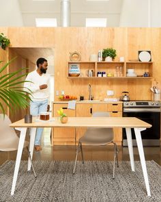 a man standing in a kitchen next to a table with chairs and a potted plant