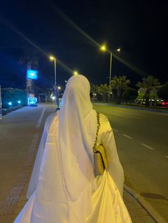 a woman dressed in white walking down the street at night with her back turned to the camera