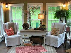 a living room filled with white furniture and lots of windows covered in shades of green