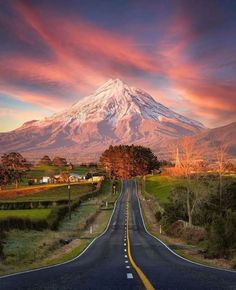 a long road with a mountain in the background and clouds above it at sunset or sunrise