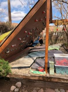 an outdoor climbing wall in the backyard with lots of rocks on it and a wooden structure