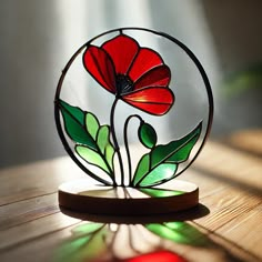 a red flower sitting inside of a glass vase on top of a wooden table next to a window