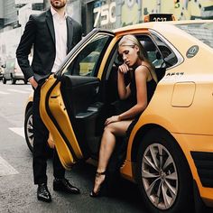 a man standing next to a woman sitting on the back of a yellow taxi cab