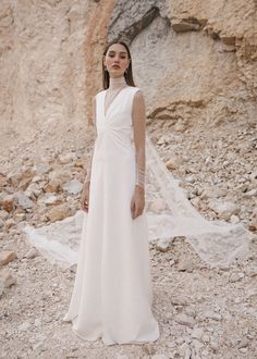 a woman in a white wedding dress standing on rocky terrain with her veil blowing in the wind