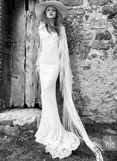 a woman in a long dress and hat standing next to an old door with her hair blowing back