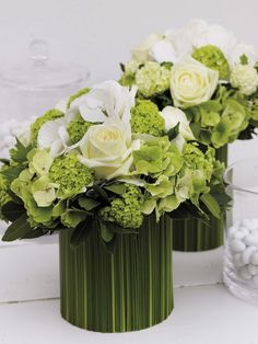 two vases filled with white and green flowers on top of a table next to each other