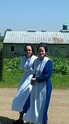 two women dressed in white and blue standing next to each other on a dirt road