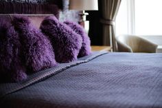 purple fluffy pillows sit on the edge of a bed