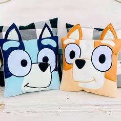 two pillows with cartoon dogs on them are sitting on a white wooden surface, one is blue and the other has an orange dog's face