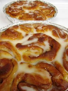 two pies sitting on top of a table covered in icing and cinnamon rolls