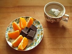 a plate with orange slices and pieces of chocolate on it next to a cup of coffee