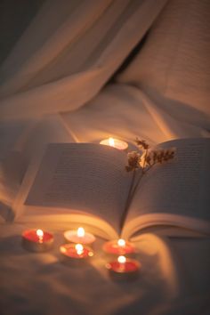 an open book sitting on top of a bed covered in candles