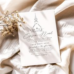 the wedding card is laying on top of some white sheets with flowers in front of it