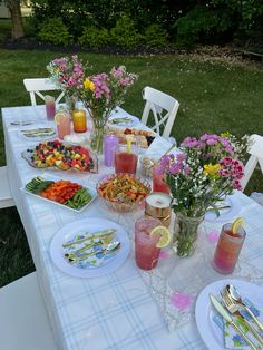 the table is set with flowers, fruit and drinks for an outdoor party or gathering