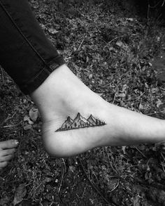 a person with a small tattoo on their foot is standing in the grass and has mountains tattooed on it