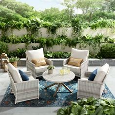 an outdoor living room with white wicker furniture and green plants on the wall behind it