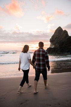 a man and woman holding hands walking on the beach near the ocean at sunset or sunrise