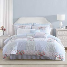 a white bed with blue and pink comforter in a bedroom next to a window