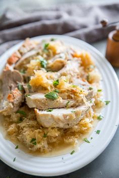 a white plate topped with meat covered in gravy and garnished with parsley