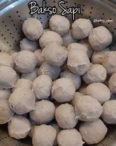 a metal bowl filled with balls of dough sitting on top of a table next to a sign that says bakso sapi