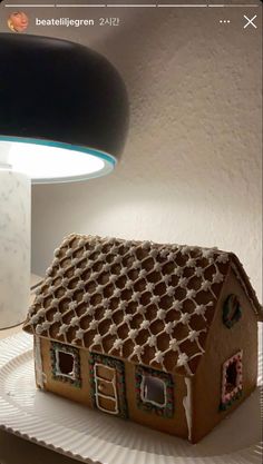 a gingerbread house is on a plate with a lamp in the corner behind it