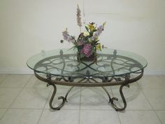 a glass table with metal legs and flowers on top is shown in front of a white wall