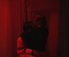 two people sitting in a room with red light coming from the window and curtains behind them