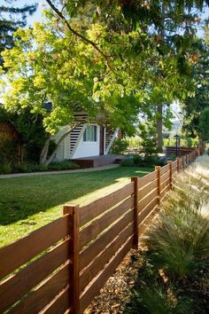 a wooden fence in front of a house with trees and grass on the side walk