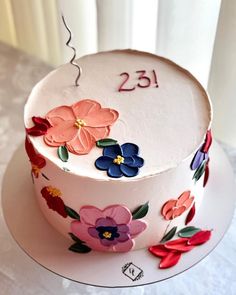 a white cake with flowers on it and the number twenty five is decorated in red, pink, blue, and purple