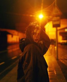 a woman standing on the sidewalk at night with her head in her hands, looking down