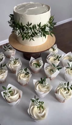 there are many cupcakes on the table with white frosting and greenery