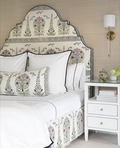 a white bed topped with lots of pillows next to a night stand