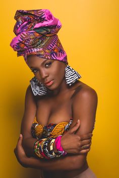 an african woman in a colorful head scarf and top with her arms crossed, against a yellow background