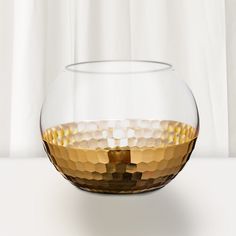 a glass bowl filled with gold liquid on top of a white countertop next to a curtain