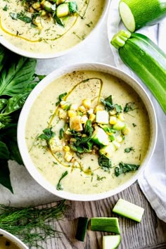 two bowls filled with soup next to cucumbers and green leafy garnish