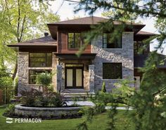 a large stone house with lots of windows and landscaping around the front yard, surrounded by lush green trees