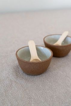 two small bowls with spoons in them on a table