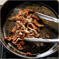 the food is being cooked in the skillet on the stove with two tongs