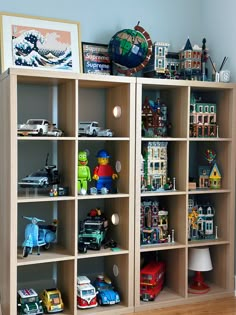 a bookcase filled with lots of toys on top of a hard wood floor next to a wall