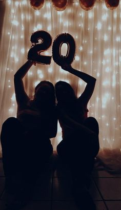 two women sitting in front of a backdrop with balloons and the number twenty on it