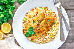 a white plate topped with chicken and rice next to lemon wedges on top of a wooden table