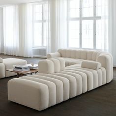 a living room filled with white furniture and large windows in the wall behind it is a coffee table that sits on top of a hard wood floor